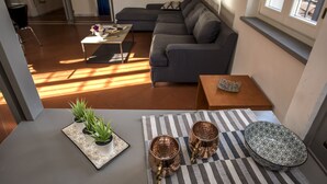 A modern living room with a sectional sofa, a coffee table, and a small wooden side table. There are three potted plants on a tray and three copper mugs on a striped tablecloth. - Ricasoli Apartment - Two Bedroom Apartment, Sleeps 4 (Firenze)