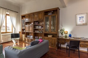 A living room with a wooden bookcase, a sofa, a desk with a chair, and a window with curtains.