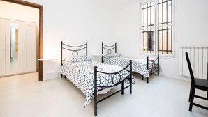 A bedroom with two beds, a window with bars, a radiator, and a door leading to another room.