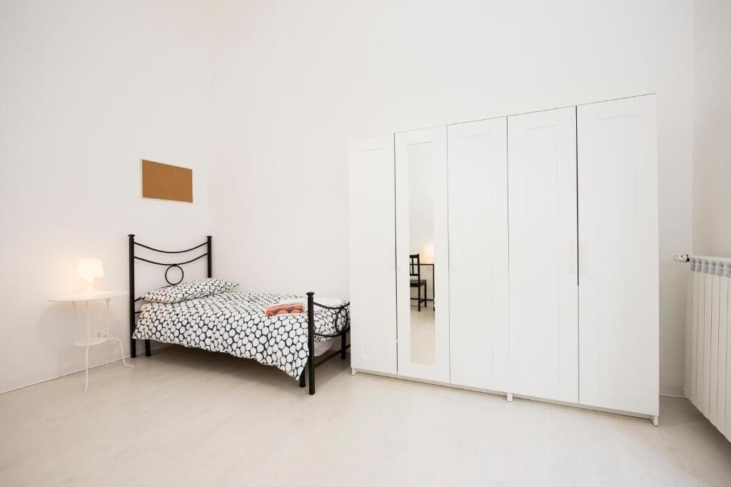 Un dormitorio con cama, un armario blanco y una mesita con lámpara.