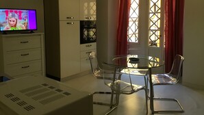 A modern room with a glass table and chairs, a television on a cabinet, and a window with red curtains. - Campidoglio T - One Bedroom Apartment, Sleeps 2 (Firenze)