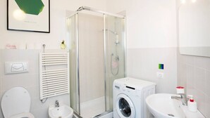 Uma casa de banho moderna com cabine de duche em vidro, máquina de lavar roupa, lavatório e sanita.