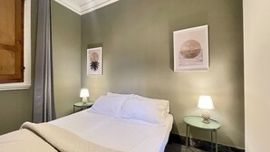 A neatly made bed with white linens in a room with green walls. There are two bedside tables with lamps, and two framed artworks on the wall. - Fortezza Fourth Floor 4 Pax (Firenze)