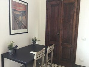 A dining area with a black table, two chairs, a framed painting, and a wooden door.