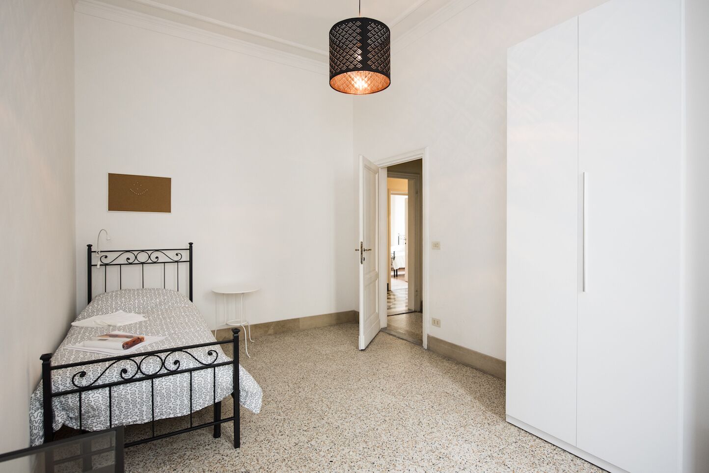 Une chambre à coucher comprenant un lit, une petite table, une armoire et un luminaire suspendu.