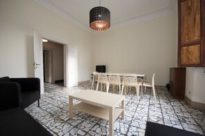A room with a stone-patterned floor, a dining table with chairs, a black sofa, and a hanging light fixture. - Fortezza Second floor (Firenze)