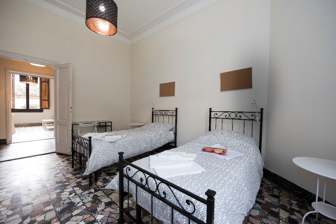 A room with two single beds, a small table, and a hanging light fixture.
