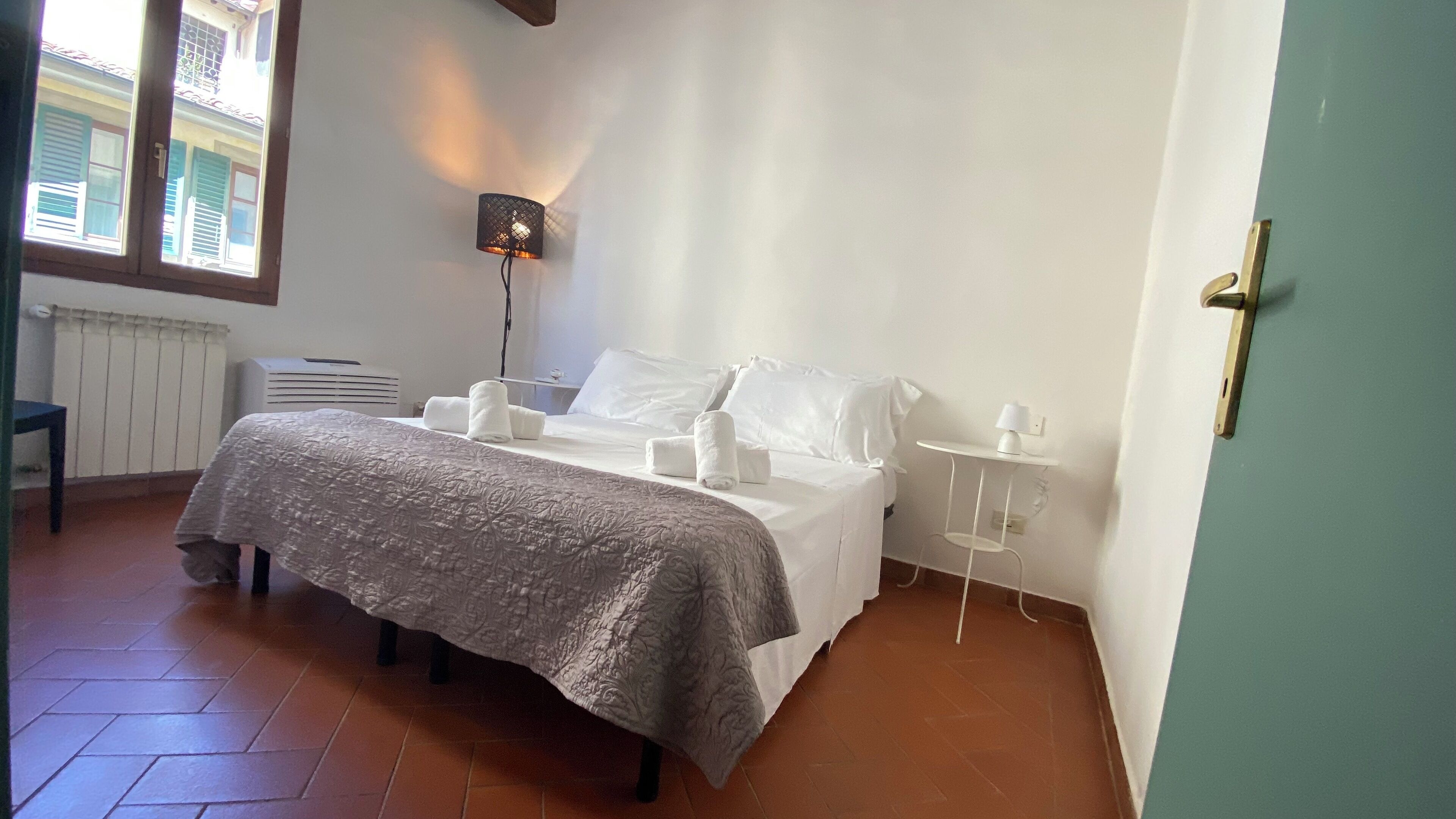 A neatly made bed with a patterned bedspread, a bedside lamp, and a small table with a lamp.