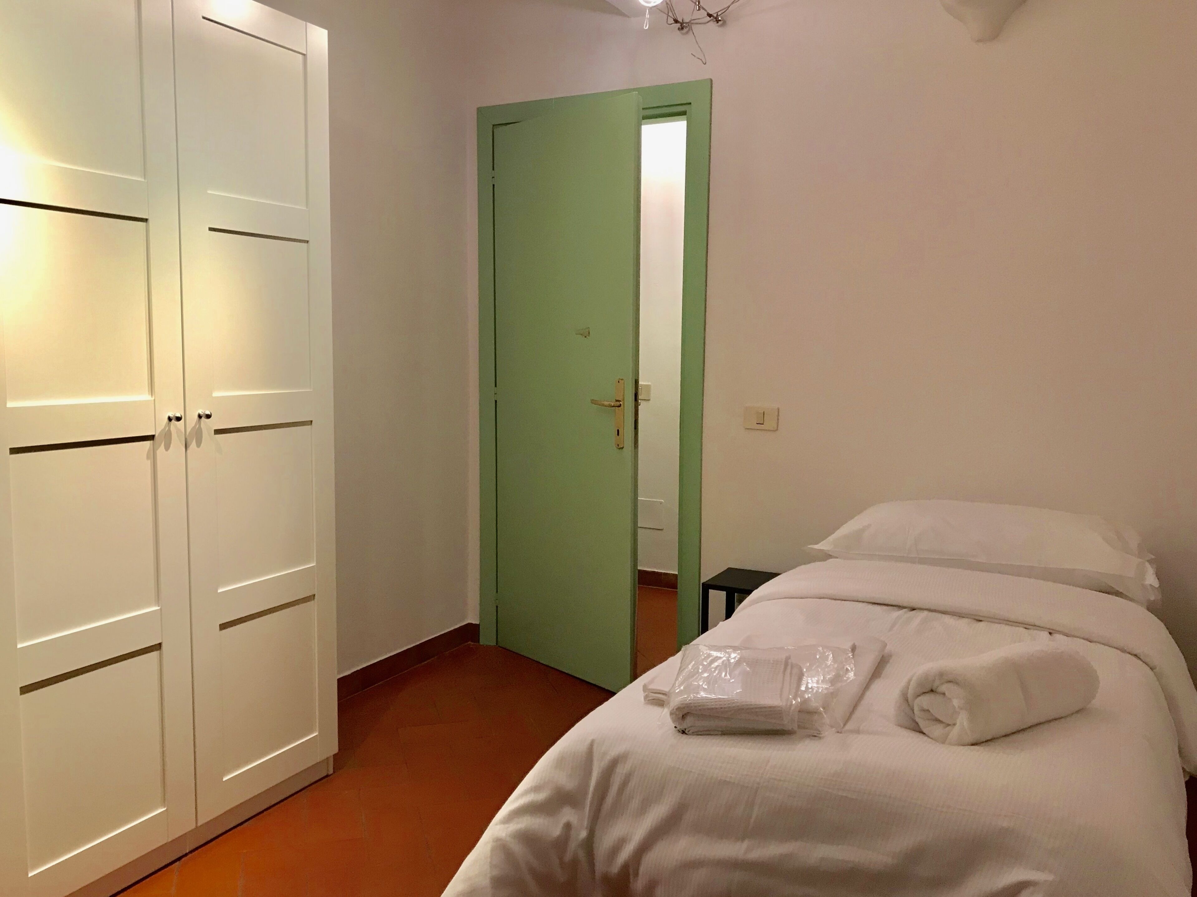 Quarto de hotel com uma cama, uma porta verde e um guarda-roupa.