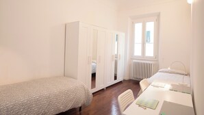 Ein kleiner, gut beleuchteter Raum mit einem Einzelbett, einem Schreibtisch mit Stuhl und einem Kleiderschrank.