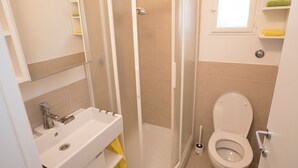 Ein kleines Badezimmer mit Dusche, Waschbecken, Toilette und Spiegel.