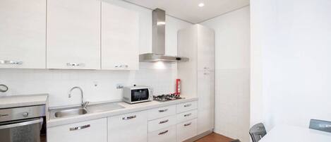 A modern kitchen with white cabinets, a stainless steel range hood, a microwave, and a gas stove.