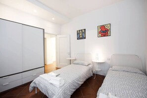 Een hotelkamer met twee eenpersoonsbedden, een kledingkast, een deur die naar een andere kamer leidt en twee kunstwerken aan de muur.
