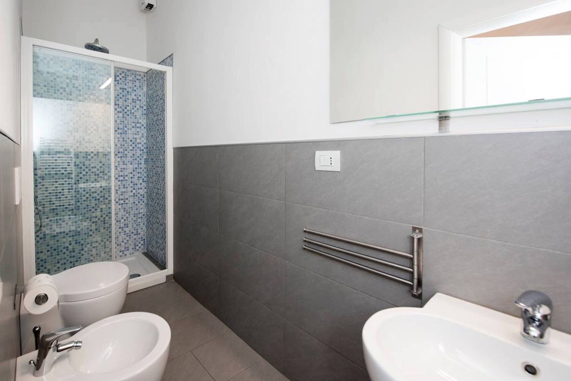 A modern bathroom with a glass shower enclosure, a toilet, bidet, and a sink.