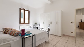 Un dormitorio con cama, una mesita con cafetera, armario y ventana.