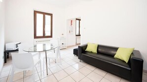 Una sala de estar moderna con una mesa de comedor de vidrio, sillas blancas, un sofá de cuero negro con cojines verdes y un radiador blanco.
