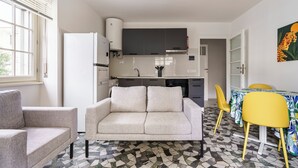 A modern kitchen with a built-in oven, a refrigerator, and a microwave. There is a dining area with a table and chairs, and a sofa in the living area. - Buonarroti Apartment (Firenze)