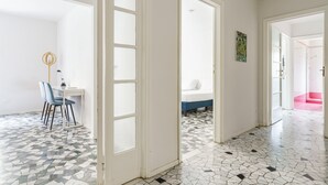 A room with a tiled floor, a bed, a desk with chairs, and a door leading to another room. - Buonarroti Apartment (Firenze)