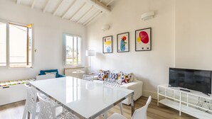 A modern living room with a white table, chairs, a sofa with colorful cushions, a TV on a stand, and abstract art on the wall. - Faenza 73 - Three Bedroom Apartment, Sleeps 5 (Firenze)
