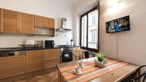 A modern kitchen with wooden cabinets, a stove, and a dining area with a striped table runner. - Faenza double - One Bedroom Apartment, Sleeps 2 (Firenze)