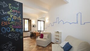 A cozy living room with a sofa, a dining area with a table and chairs, and a wall with a city skyline mural. - Faenza double - One Bedroom Apartment, Sleeps 2 (Firenze)