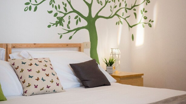 A bedroom with a bed, pillows, a nightstand, and a wall mural of a tree. - Faenza double - One Bedroom Apartment, Sleeps 2 (Firenze)