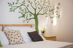 Un dormitorio con cama, almohadas, una mesita de noche y un mural de un árbol en la pared.