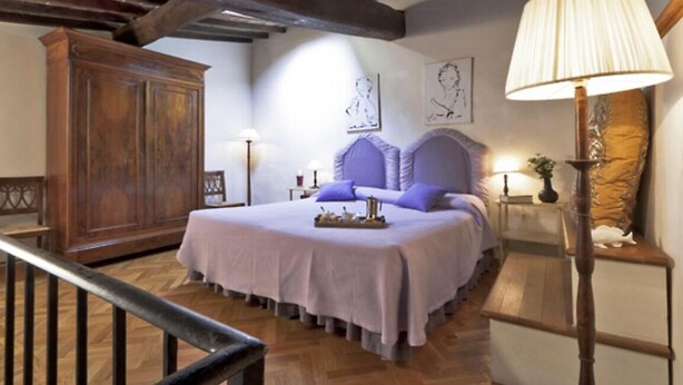 Une chambre à coucher avec une grande armoire en bois, un lit recouvert d’une couvre-lit de couleur claire et une table de chevet avec une lampe.