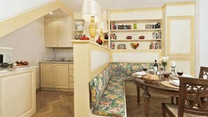 Une cuisine avec un banc en bois, une table à manger dressée pour quatre personnes et une bibliothèque remplie de livres et d’objets décoratifs.