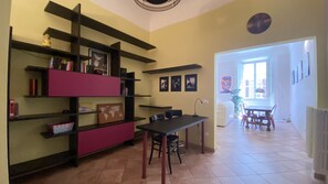 A dining area with a table and chairs, a bookshelf with various items, and a view of the dining room through an open doorway. - Battistero Apartment (Firenze)