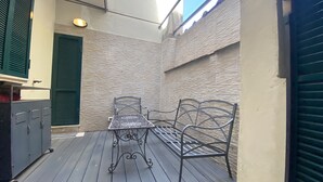 A small outdoor patio with a metal table and two chairs, a green shuttered door, and a textured wall. - Battistero Apartment (Firenze)