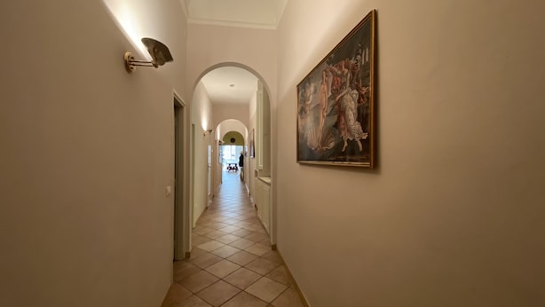 A hallway with a tiled floor, a painting on the wall, and a door at the end. - Battistero Apartment (Firenze)