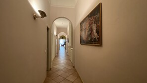 A hallway with a tiled floor, a painting on the wall, and a door at the end. - Battistero Apartment (Firenze)