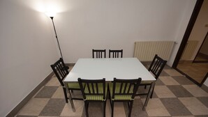 Zona pranzo con tavolo bianco e sei sedie, una lampada da terra e un termosifone.