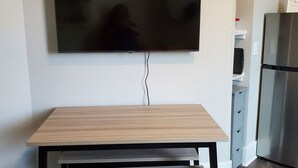 Una sala moderna con una mesa de comedor de madera, un televisor de pantalla plana montado en la pared y un refrigerador de acero inoxidable.