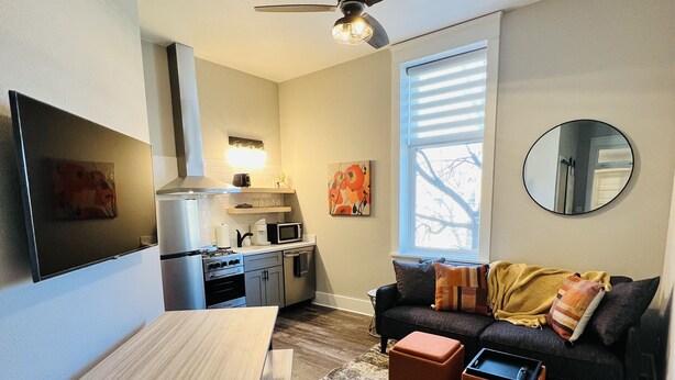 Un espacio habitable compacto con kitchenette, zona de comedor y área de estar con sofá y pufs.