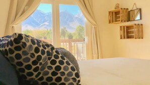 A bedroom with a bed, curtains, and a view of mountains through a window. - >>MAGICAL property on 5 acres in the Alabama Hills (Lone Pine)