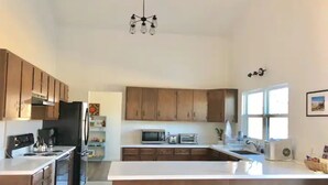 A modern kitchen with wooden cabinets, a central island with red stools, a microwave, and a sink. - >>MAGICAL property on 5 acres in the Alabama Hills (Lone Pine)