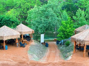 A campsite with thatched-roof huts, picnic tables, and chairs. - Son's Guadalupe Glamping Tent F (New Braunfels)