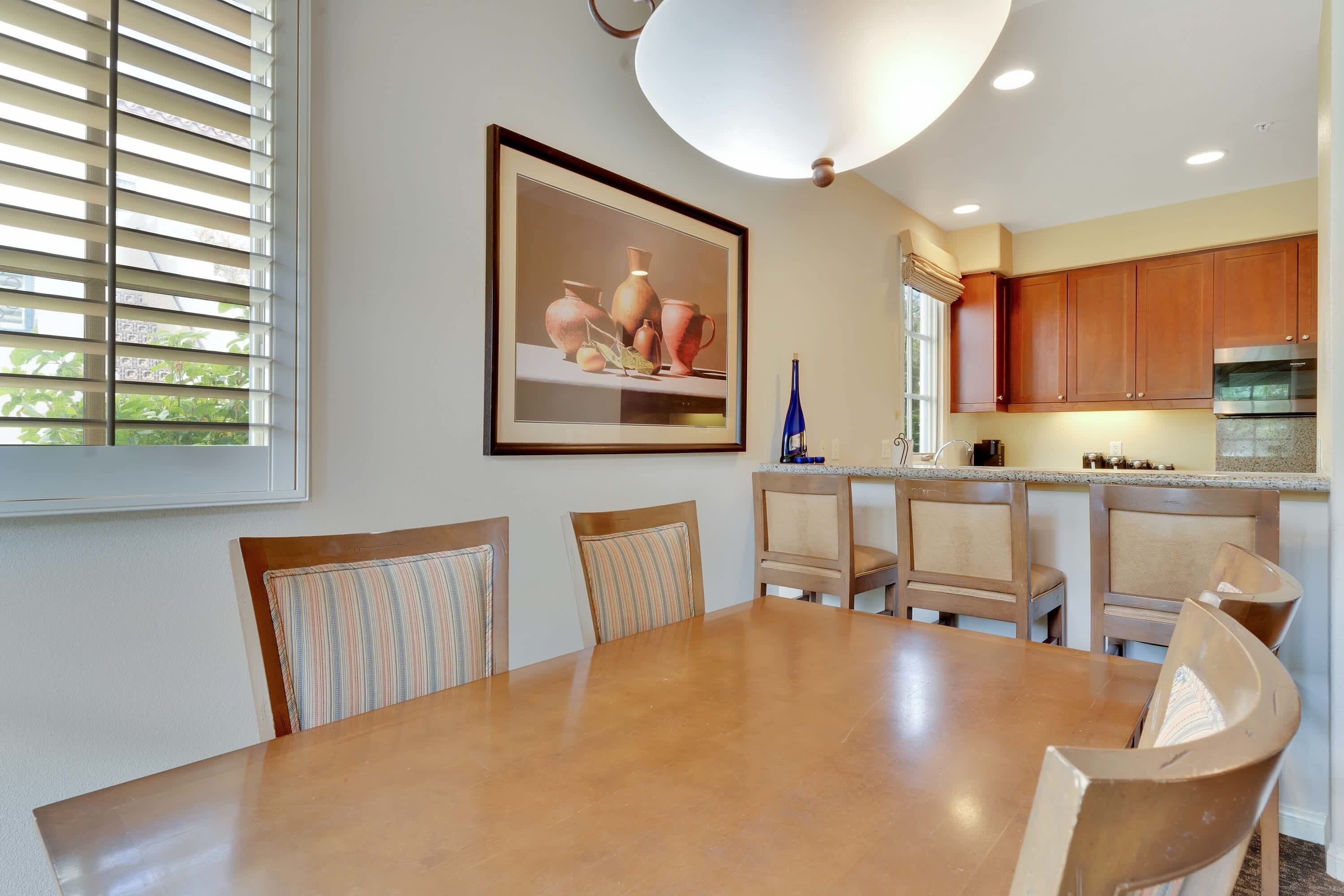 A dining area with a wooden table and chairs, a kitchen with wooden cabinets, and a framed artwork on the wall.