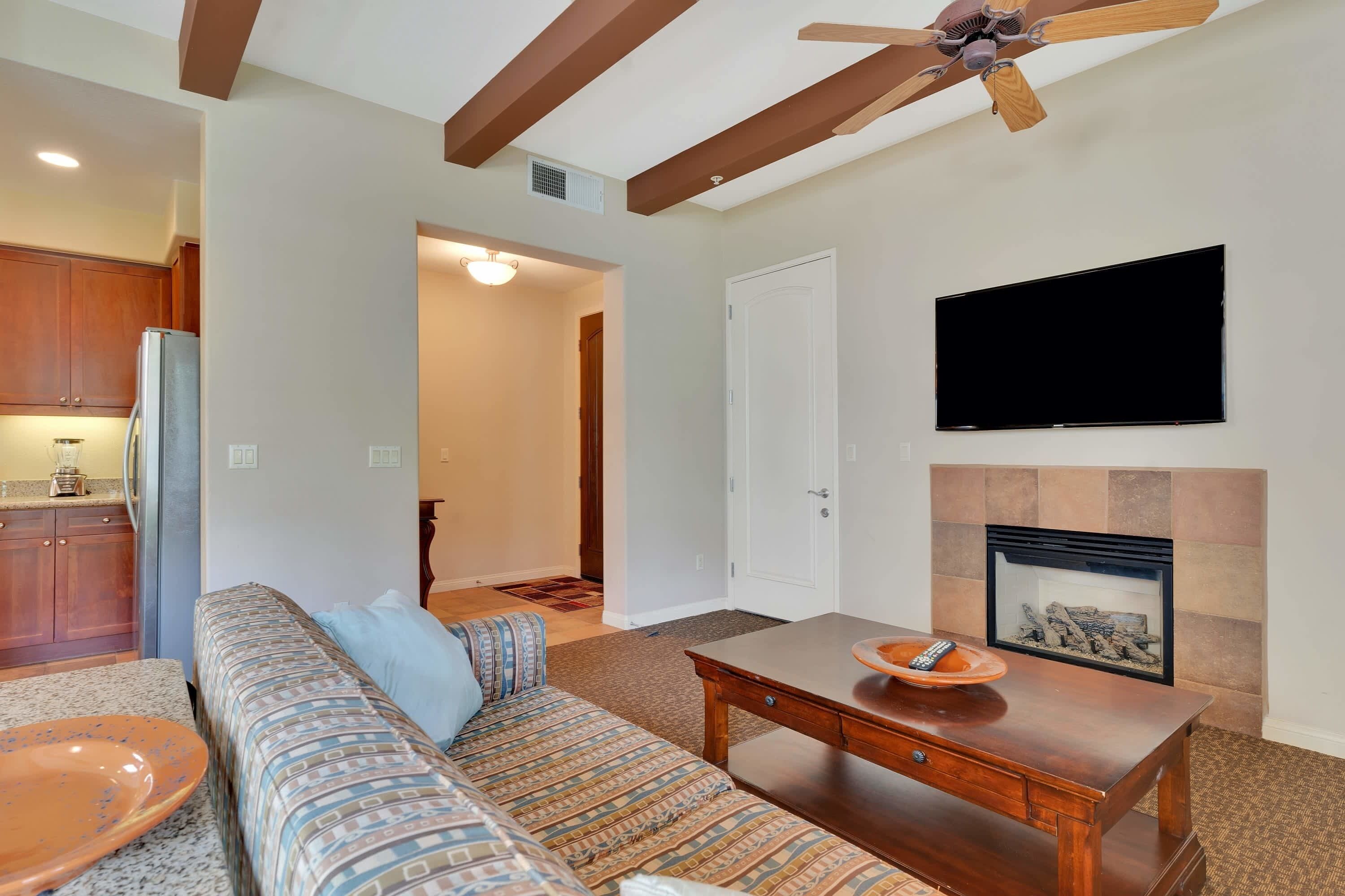 A living room with a sofa, coffee table, fireplace, TV, and kitchen area.