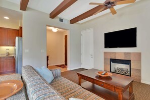 A living room with a sofa, coffee table, fireplace, TV, and kitchen area.