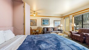 Ein Schlafzimmer mit Bett, Schreibtisch, Stuhl, Sofa und einem Fenster mit Blick auf Bäume.