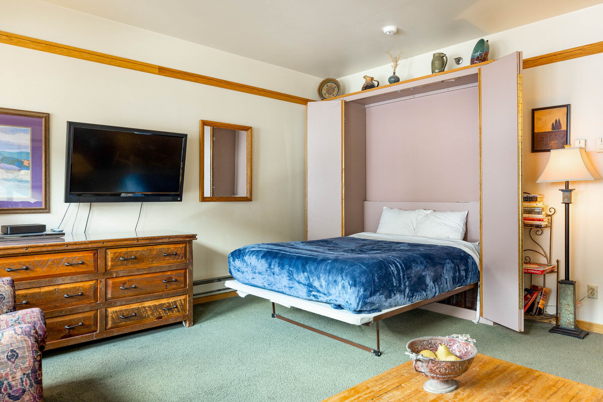 A bedroom with a bed, a dresser, a television, and a lamp.