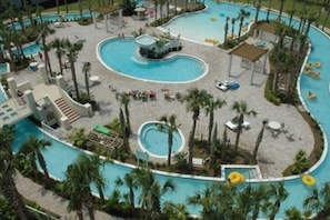 A large, winding pool with multiple sections, surrounded by palm trees and lounge areas. - Destin Festival!!  Sept 24 - 28 Available (Fort Walton Beach)