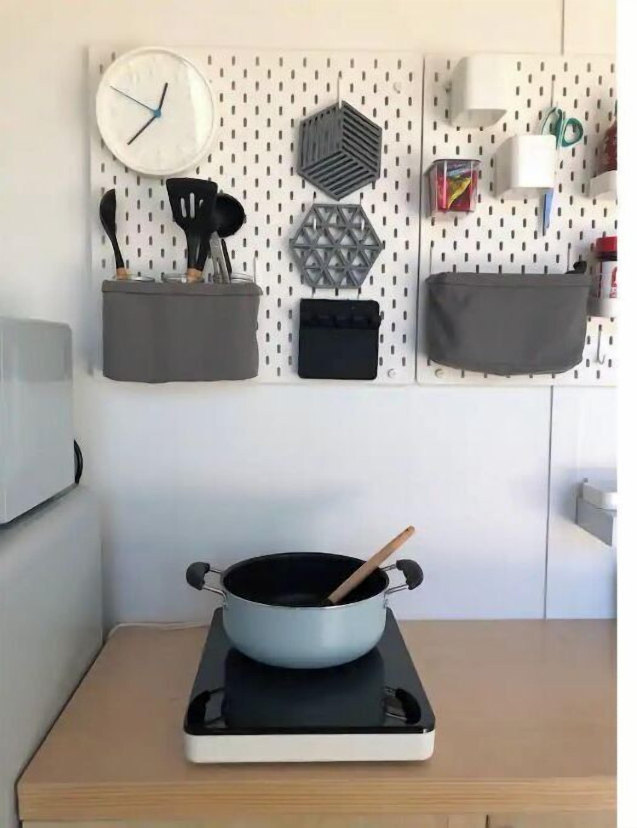 A kitchen with a pot on a portable stove, a wall-mounted clock, and organized storage with hooks and containers.