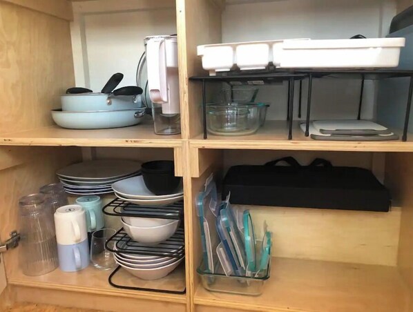 A kitchen cabinet with shelves containing dishes, bowls, a coffee maker, and utensils. - "TINY" HOME w/ expansive views of the Sierras NOW W/ WIFI! (Lone Pine)