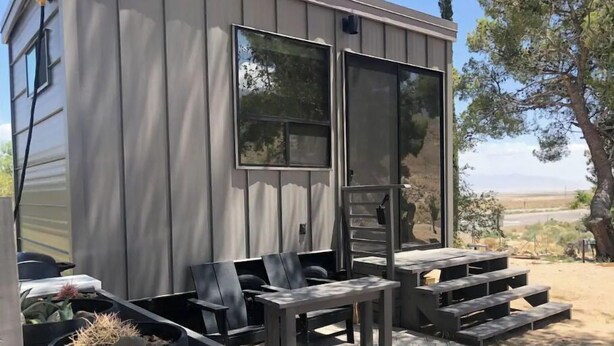A modern, compact cabin with a patio area featuring a fire pit, seating, and a view of the surrounding landscape.
