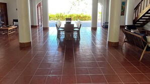 Un espacio interior amplio con una mesa central y sillas, rodeado de pilares y vistas a zonas verdes.