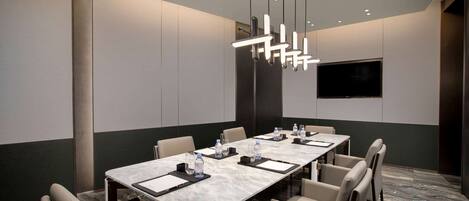 A conference room with a long table, chairs, a flat-screen TV, and pendant lighting.